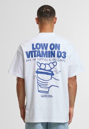 Camiseta de algodón blanca con texto gráfico azul e ilustraciones de una mano sosteniendo una taza de café con croissants encima. Corte casual.