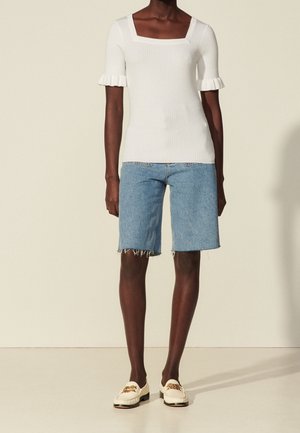 Weißes, geripptes Kurzarmoberteil mit quadratischem Ausschnitt, kombiniert mit blauen Denim-Shorts mit ausgefransten Kanten und beigefarbenen Loafers mit dekorativen Akzenten.