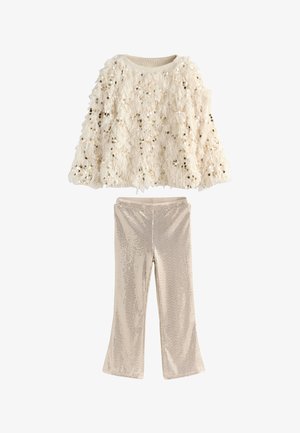 Dječja odjeća u dva dijela koja uključuje kremasti prsluk s resicama ukrašenim šljokicama i pripadajuće proširene hlače s teksturiranim metalik završetkom.