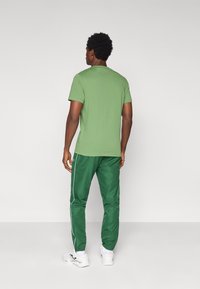 Camiseta de algodón verde de manga corta combinada con pantalones deportivos verdes con rayas blancas laterales y puños elásticos, usada con zapatillas blancas.