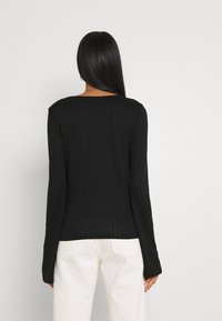 Schwarzes, geripptes Langarmoberteil mit Rundhalsausschnitt, taillierter Silhouette und strukturiertem Muster. Kombiniert mit cremefarbenen Hosen.