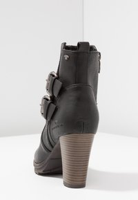 Bottine noire en cuir synthétique texturé avec deux boucles argentées, un talon robuste rayé marron et un bout arrondi.