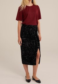 Burgundy t-shirt med korta ärmar, kombinerad med en figursydd svart paljettmidikjol med en hög slits. Svarta platta skor.