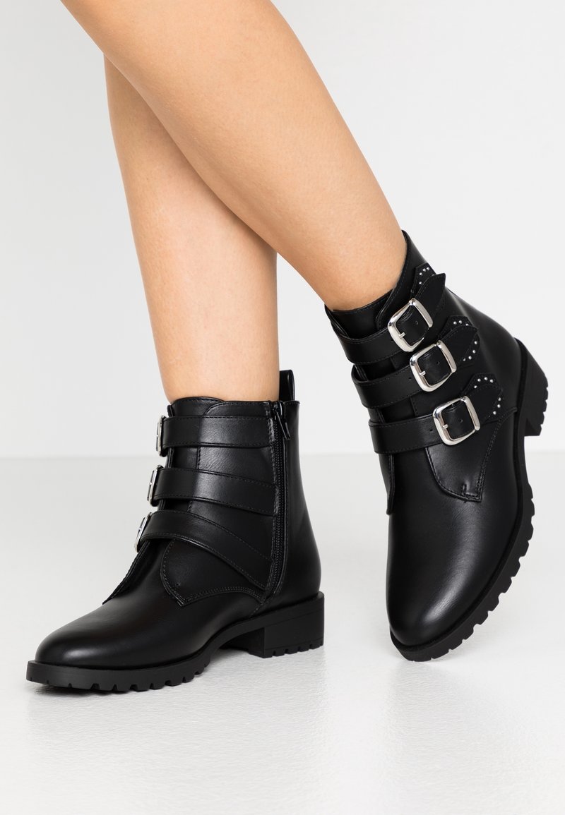Svarta läderankelstövlar med tre justerbara spännen, en texturerad panel och en låg, tjock klack. Tjock, mönstrad sula för bra grepp.