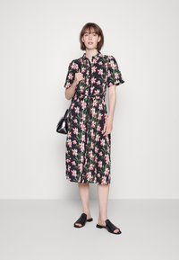 Vestido midi floral com mangas curtas, fundo preto, flores vibrantes em rosa e verde, frente com botões, cintura ajustada, combinado com mules pretos.