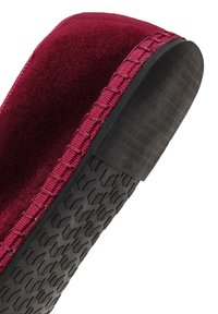 Gros plan de la semelle et du bord latéral d'un chausson bourgogne avec une semelle en caoutchouc noir texturé et un bord en tissu.