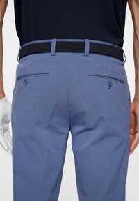 Blaue gemusterte Hosen bestehen aus einem strukturierten Stoff, haben zwei Gesäßtaschen mit Knopfverschlüssen und einen gewebten schwarzen Gürtel.