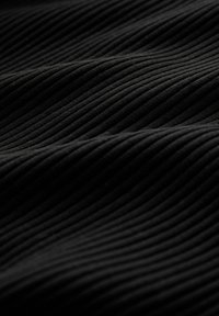 Tejido negro acanalado con una superficie texturada, que presenta secciones alternas elevadas y planas que crean un patrón en forma de ola.