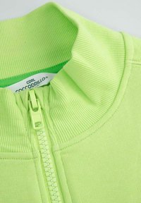 Jasnozielona kurtka na zamek błyskawiczny o żeberkowanej fakturze i z podwyższonym kołnierzem. Posiada dopasowany zamek oraz metkę oznaczoną "CDRL Coccodrillo."