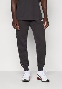 Sive trenirke s slim fit krojem, belim stranskim pasom in rebrastimi manšetami, v kompletu z belimi športnimi copati z rdečimi poudarki. Standarden bombažni material.