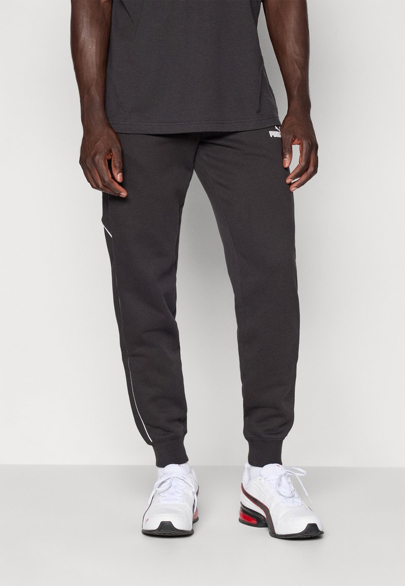 Sive trenirke s slim fit krojem, belim stranskim pasom in rebrastimi manšetami, v kompletu z belimi športnimi copati z rdečimi poudarki. Standarden bombažni material.