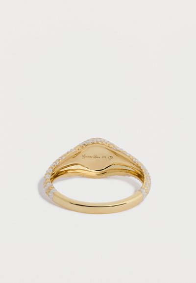 Złoty pierścionek z plecionym wzorem, ozdobiony przezroczystymi akcentami. Gładkie wnętrze z wygrawerowaną nazwą marki i próbą metalu.