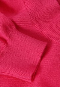 Pull en maille rose vif avec poignets et encolure côtelés. Texture lisse avec une finition douce, mettant en valeur les détails du fil fin.