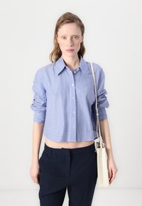 Blue and white striped button-up shirt with cropped design, long sleeves rolled up, paired with navy pants and a beige handbag.