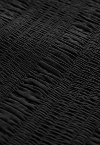 Gros plan sur un tissu noir avec des rangées de fronces cousues créant des rayures verticales texturées.