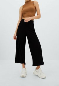 Zwarte geribbelde broek met wijd been gecombineerd met een aansluitend bruin mouwloos topje en witte chunky sneakers. Gestructureerde stof met een ontspannen pasvorm.