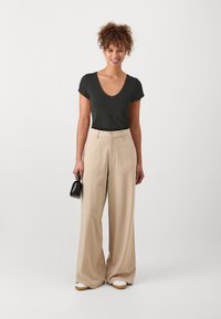T-shirt noir à col en V, pantalon beige à jambes larges, baskets blanches, sac à main noir. Tissu lisse, coupe décontractée, et détails subtils sur le pantalon.