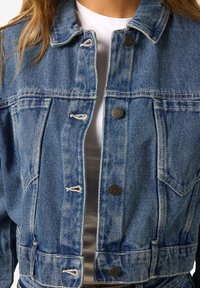 Zils denims īsais jaka ar pogu aizvēršanu, divām krūšu kabatām un plīsušo apakšmalu. Iespiež klasisku apkakli un izbalējušu tekstūru.