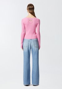 Prilagođena roza rebrasta dukserica s dugim rukavima, koja na leđima ima akcent s logotipom. Uparena s svijetloplavim širokim trapericama.