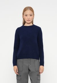 Pulover tricotat bleu marin cu guler rotund, mâneci lungi și tiv ribbit. Textură uniformă, formă ajustată. Asortat cu pantaloni cargo gri.