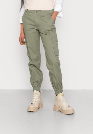 Olijfgroene cargo broek met elastische boorden en zijzakken, gemaakt van duurzaam materiaal. Gecombineerd met beige chunky laarzen.