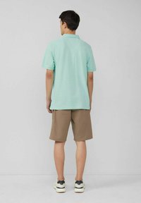 Polohemd in mintgrün mit kurzen Ärmeln, kombiniert mit beigen Shorts. Das Outfit wird mit Sneakers in einem Schwarz-Weiß-Farbschema ergänzt.