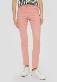 Jeans ajustados rosa hechos de algodón, con un clásico diseño de cinco bolsillos y cierre de botón. Combinados con zapatillas blancas para el contraste.