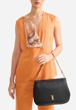 Donna che indossa un abito senza maniche arancione con un dettaglio a sciarpa marmorizzata, che tiene una borsa in pelle nera con una tracolla e una chiusura dorate.