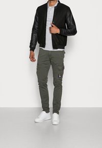 Schwarze Bomberjacke mit Lederärmeln, graues Polohemd, olivfarbene Cargo-Hosen mit Taschen und weiße Sneakers. Schlichte, lässige Kleidung.