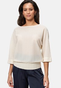 Pull en tricot couleur crème avec un motif de vagues texturé, encolure large, manches trois-quarts et coupe décontractée.