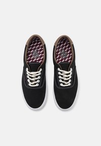 Czarne tenisówki na płótnie z brązowym skórzanym akcentem, białą gumową podeszwą i kremowymi sznurowadłami. Wnętrze zdobi czerwono-biały wzór z logo.
