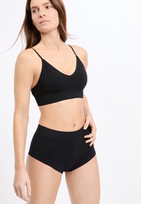 Schwarzer nahtloser BH mit V-Ausschnitt und verstellbaren Trägern, kombiniert mit hoch taillierten schwarzen nahtlosen Slips. Strukturiertes Gewebe mit einem dezenten Muster.