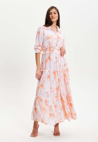 Maxi dress made of lightweight fabric, featuring a white base with orange tie-dye, buttoned front, smocked waist, and tiered ruffles.