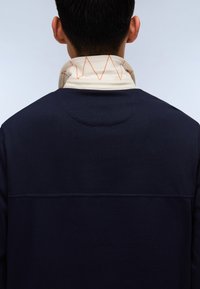 Sudadera marina con alto cuello y una bufanda crema con costuras en zigzag naranjas. Textura suave con detalles de diseño en capas.