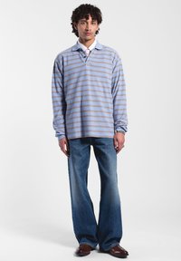 Lichtblauw langemouw polo met horizontale bruine strepen, gecombineerd met wijde blauwe denim jeans en bruine nette schoenen.