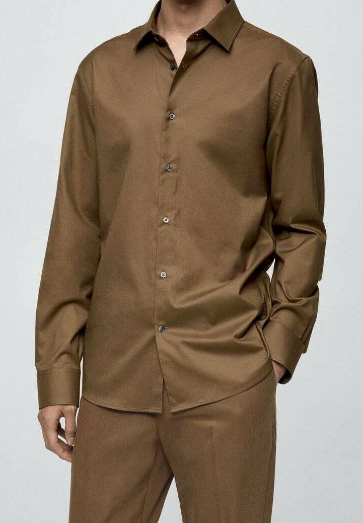 Homme portant une chemise marron à manches longues boutonnée et un pantalon marron assorti, une main dans la poche et l'autre détendue.