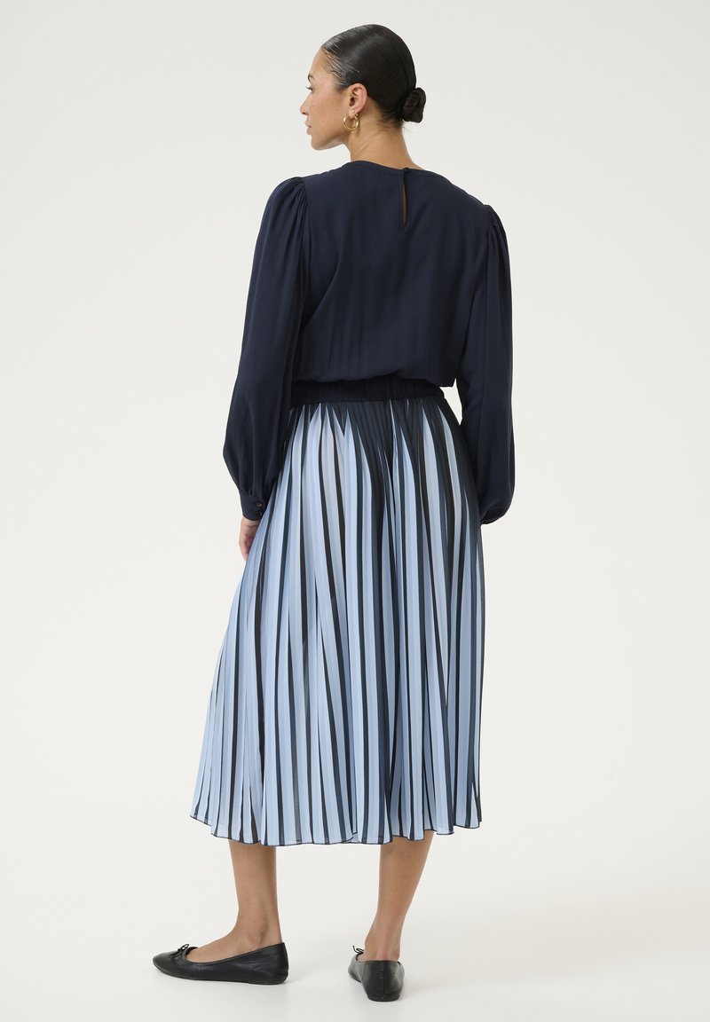 Tume sinise varrukatega pluus, mida on kombineeritud helesinise ja tumesinise triibulise plisseeritud midi seelikuga. Mustad sileda tallaga kingad täiendavad välimust.