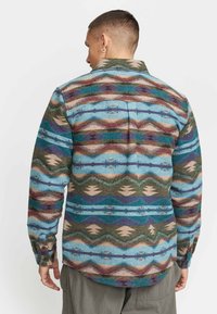 Gepatterneerde flanellen shirt met een golvend ontwerp in blauw, groen en kastanjebruin, voorzien van een kraag en knopenmanchetten. Textuur van de stof is zichtbaar.