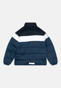 Doudoune bleu marine, avec des rayures blanches et noires. Fabriquée en matériau brillant et matelassé, avec un col montant et des poignets élastiques.
