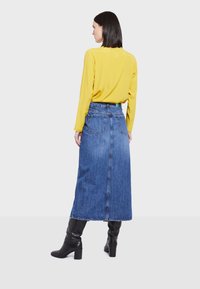 Denim maksi suknja s dva stražnja džepa, nosi se s dugim žutim topom i crnim čizmama s potpeticom. Suknja ima definiranu liniju struka.