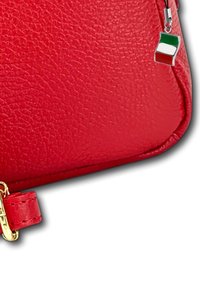 Rode faux leren portemonnee met een getextureerd oppervlak, gouden hardware en een bedeltje met de Italiaanse vlag. Compacte en rechthoekige vorm.