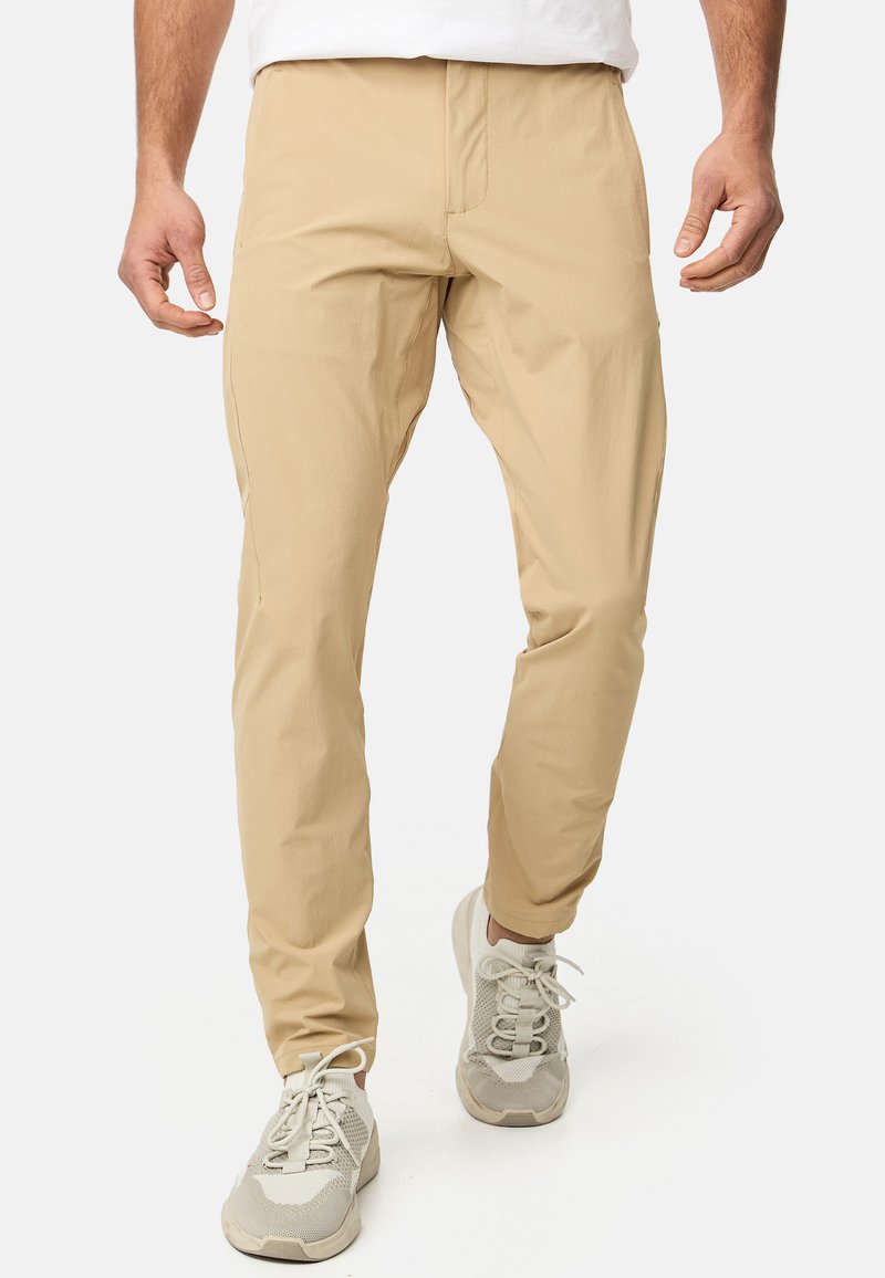 Pantalons légers beige à coupe fuselée, avec une texture lisse et des coutures subtiles. Associés à des chaussures de sport grises.