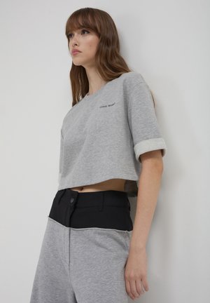 Sweatshirt grigio corto con scollatura tonda e maniche arrotolate. Pantaloni neri a vita alta con chiusura a bottone e tessuto grigio a contrasto.