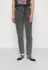Jeans de mezclilla negros con un corte de pierna recta, que presentan una cintura alta y una sutil textura descolorida. Combinados con zapatillas negras y blancas.