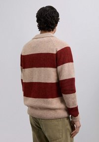 Suéter de punto en beige con llamativas franjas rojas. Ribete en el dobladillo y el cuello, presentando un corte relajado. Vista trasera, que muestra el diseño a rayas.