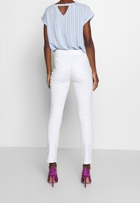 Jeans blancos ajustados combinados con una camisa de rayas azul claro con un corte en la espalda, complementados con zapatos de tacón fucsias.