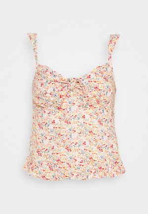 Bezrękawny kwiatowy crop top z cienkimi ramiączkami, wiązaniem z przodu i małymi czerwonymi, pomarańczowymi i niebieskimi kwiatami na jasnym tle.