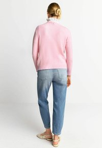 Hellrosa Pullover mit strukturiertem Finish und einem gerafften weißen Kragen, kombiniert mit blauen Denim-Jeans und hellen Schuhen.
