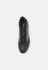 Pantofii atletici negri, cu un material superior texturat, prezentând dungi verticale, șireturi negre și accente aurii. Design aerodinamic și vârf rotunjit.