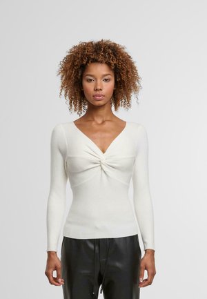 White ribbed long-sleeve top featuring a deep V-neckline and twisted knot detail at the front, paired with black leather pants.